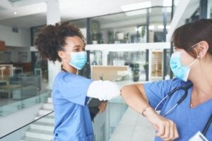 Masked Medical Assistants Greet Each Other By Bumping Elbows