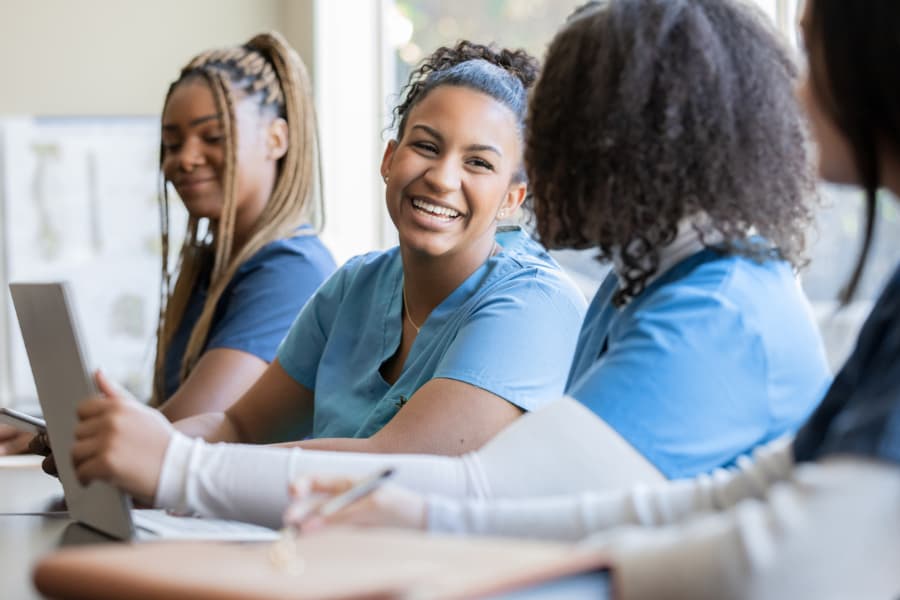 Smiling students wearing blue scrubs and sitting at table in classroom