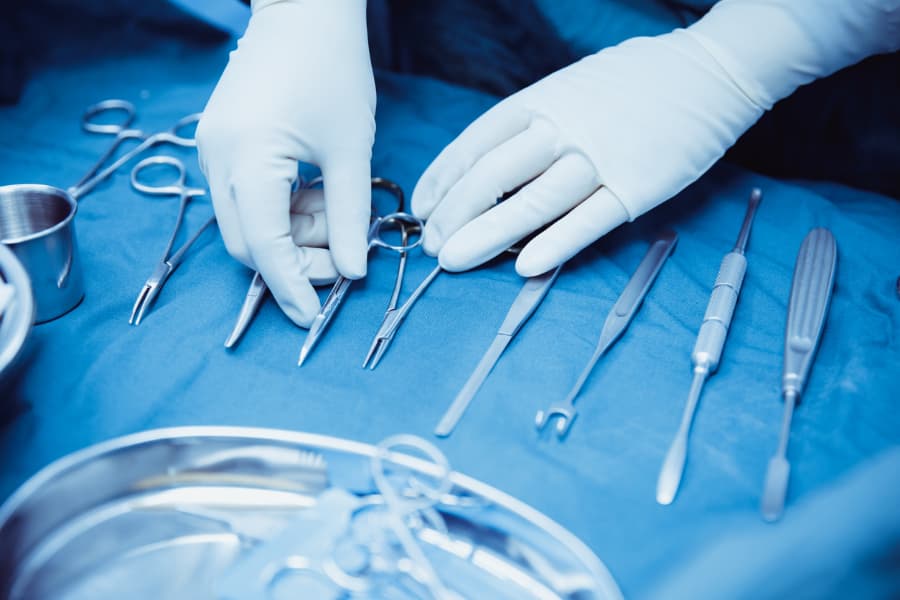 Medical assistant organizing surgical utensils in preparation for plastic surgery procedure 